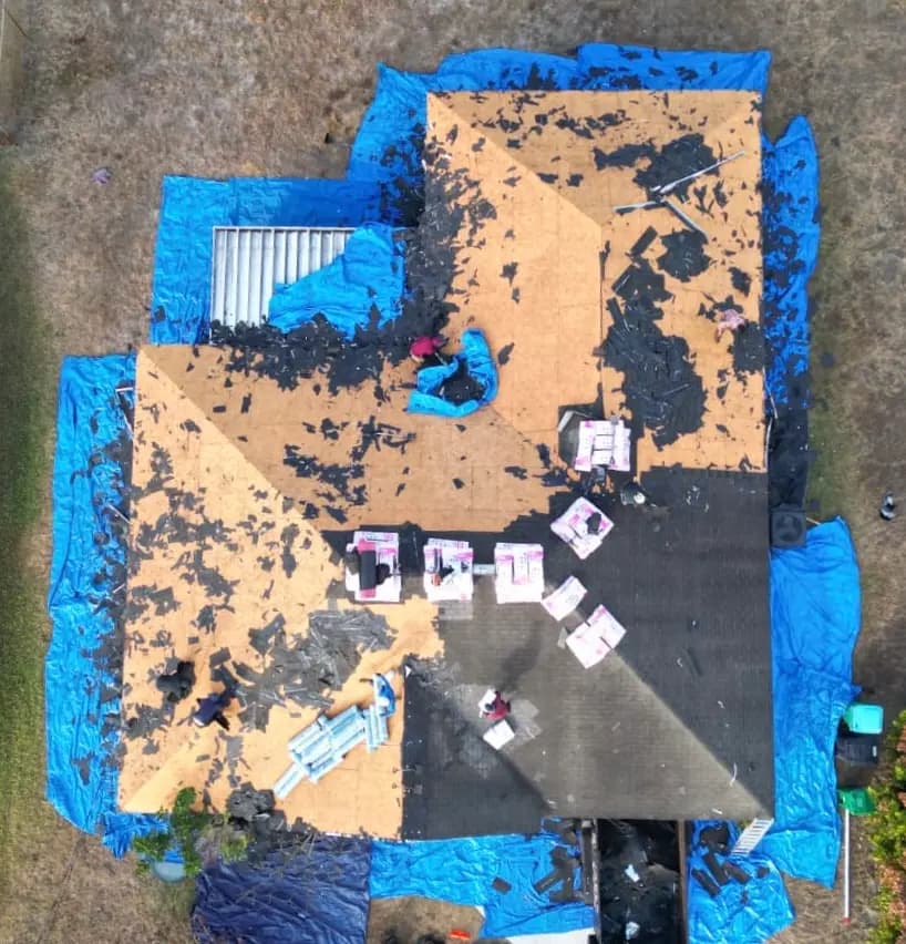 Shingle tear-off — exposed deck, pink bundles, blue yard tarps