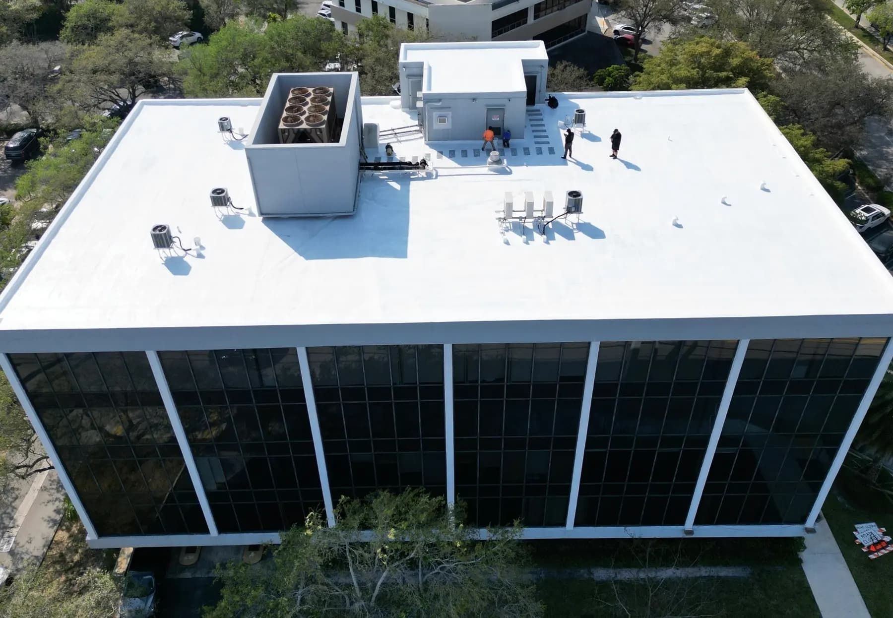 White low-slope commercial roof with HVAC and crew on deck