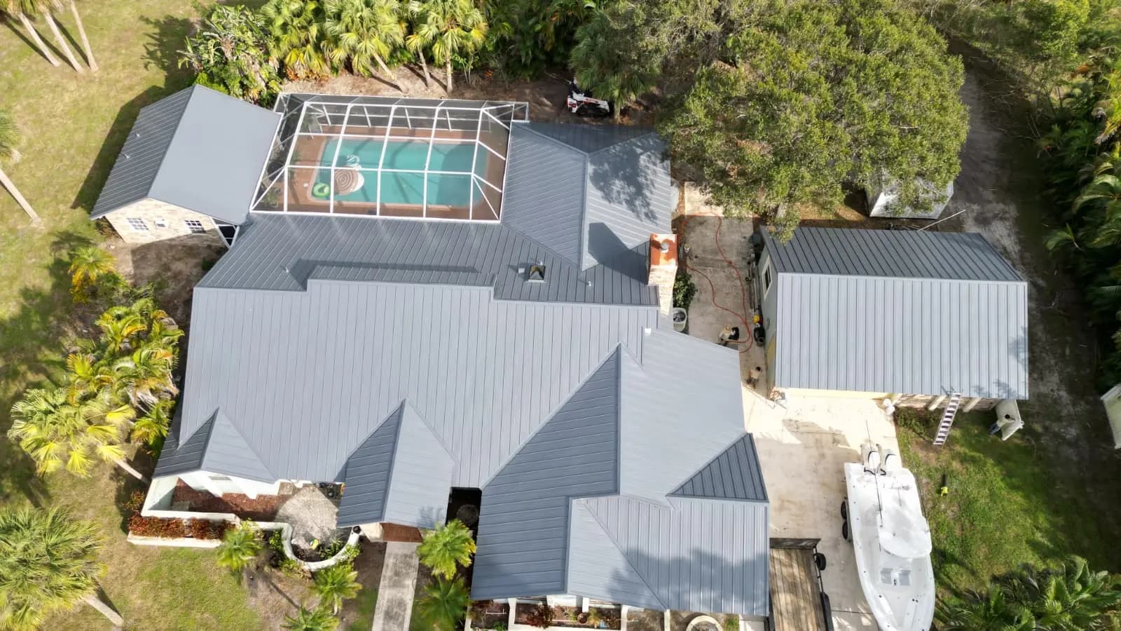 Charcoal standing-seam metal roof on a large estate with pool cage and palms